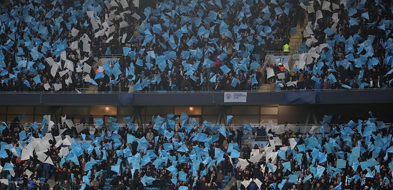 man city fans waving blue and white flags in crowd